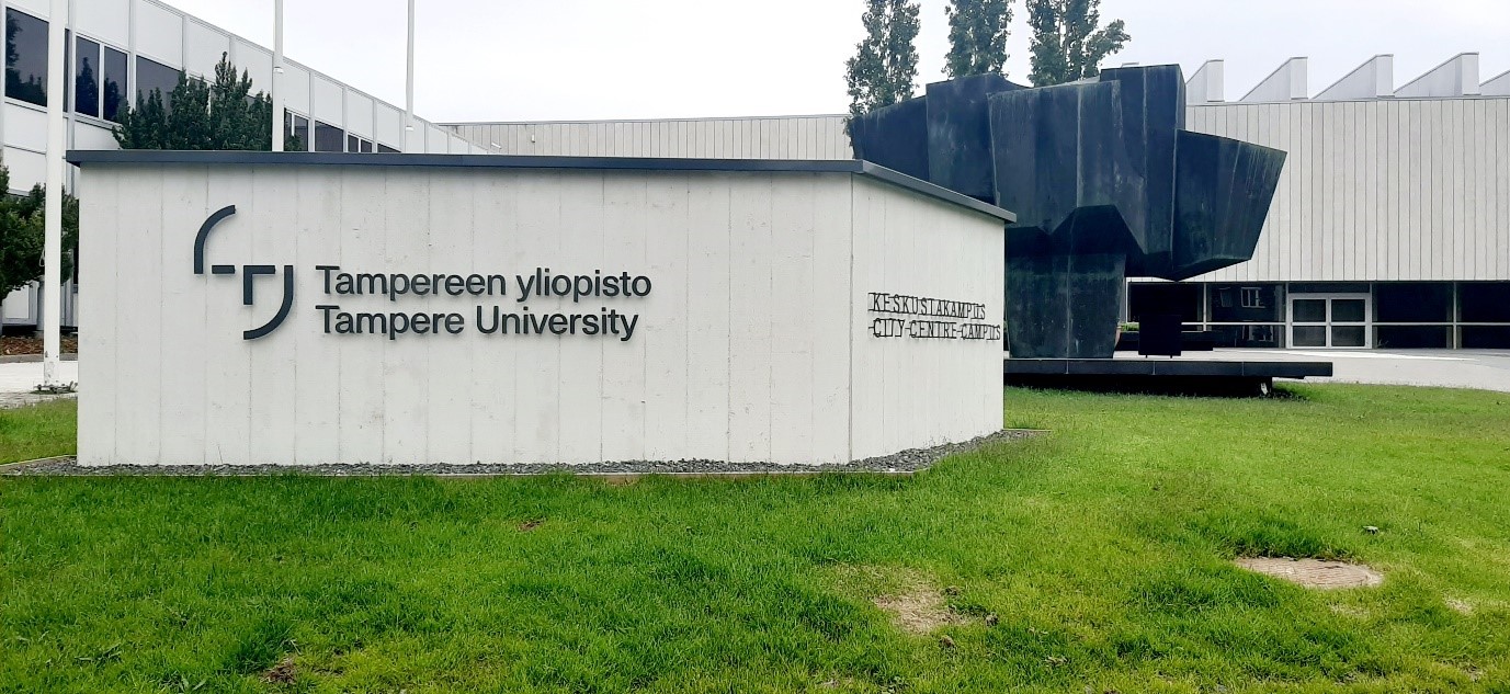 yliopiston logopaasi Päätalon edessä, vihreää nurmea