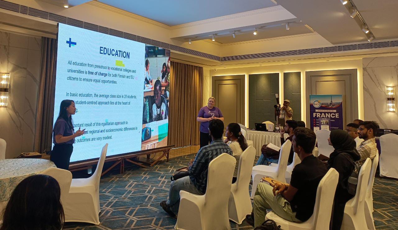 Two people presenting in a classroom with headline "Education" on the screen.
