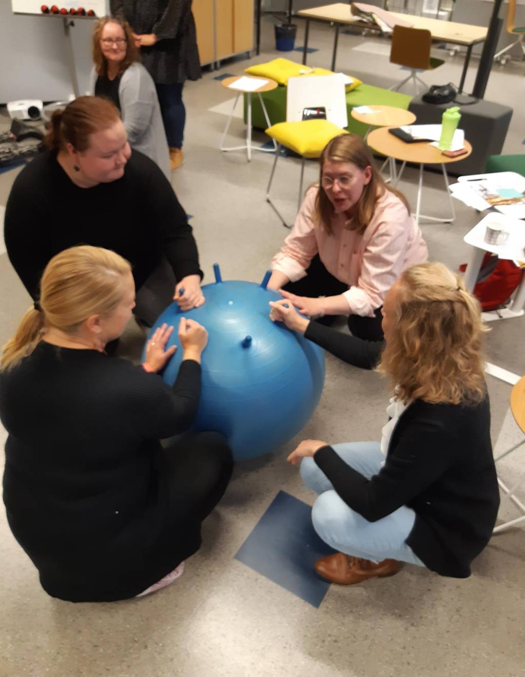 Neljä ihmistä sinisen jumppapallon ympärillä. Kuva Taidot elämään -koulutuksesta.