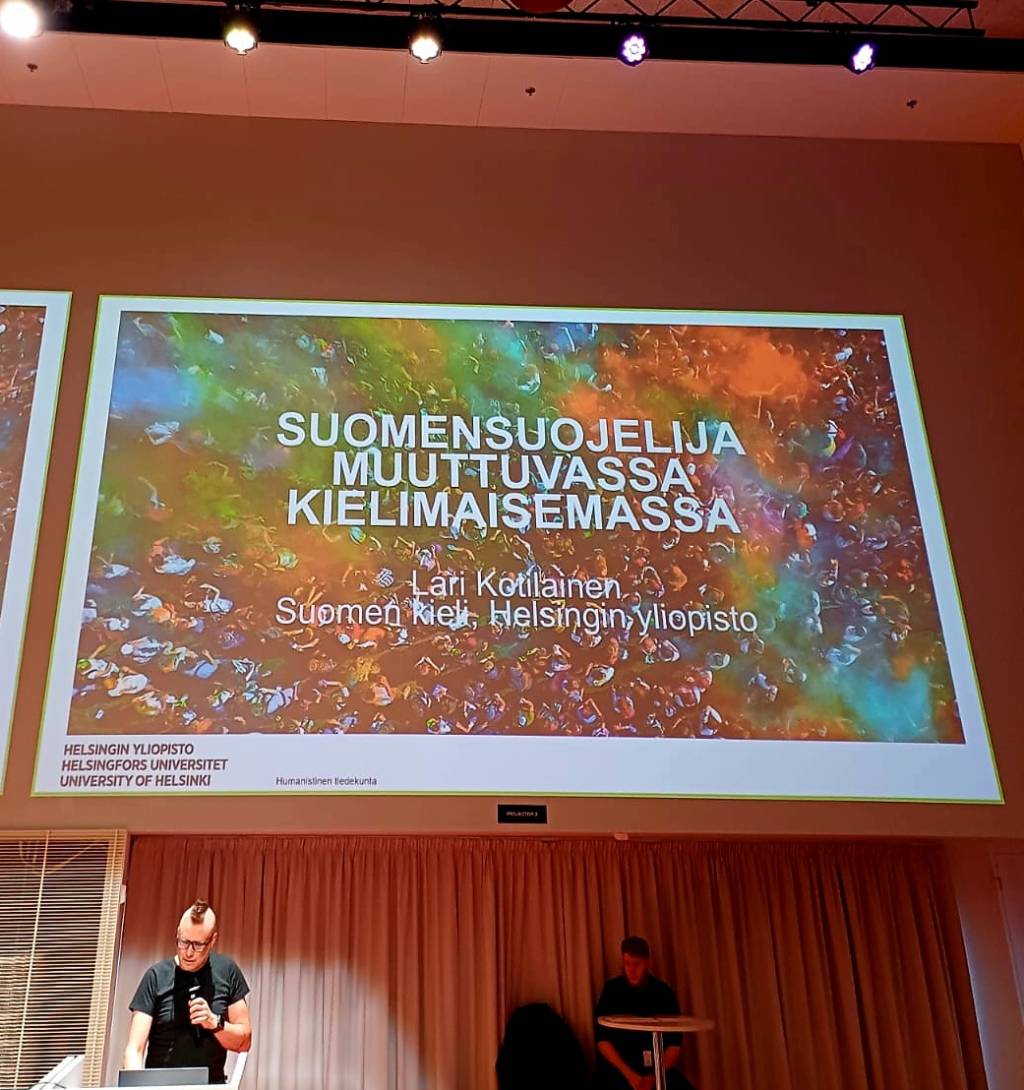 Mies puhumassa lavalla mikrofoniin.
