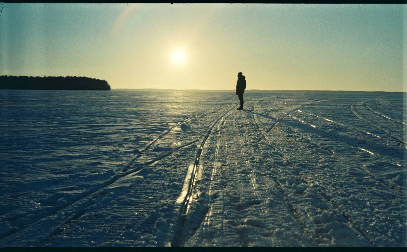 A silhouette of a person walking on a frozen lake, illuminated by the warm hues of a sunset in the background.