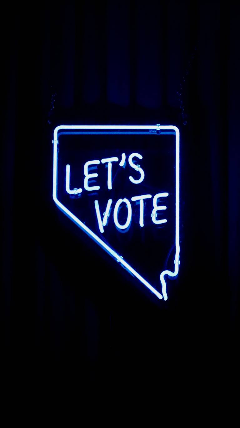 Kuva, jossa musta tausta ja valoputkista luotu puhekupla, jossa lukee Let`s vote eli suomeksi äänestetään