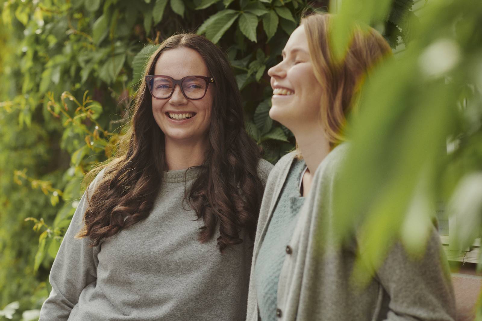 Kaksi hymyilevää naista puiden siimeksessä.
