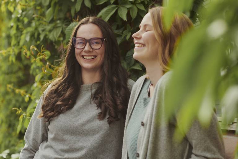 Kaksi hymyilevää naista puiden siimeksessä.