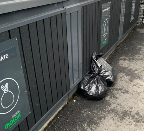 a grabage bag sitting outside of a dumpster