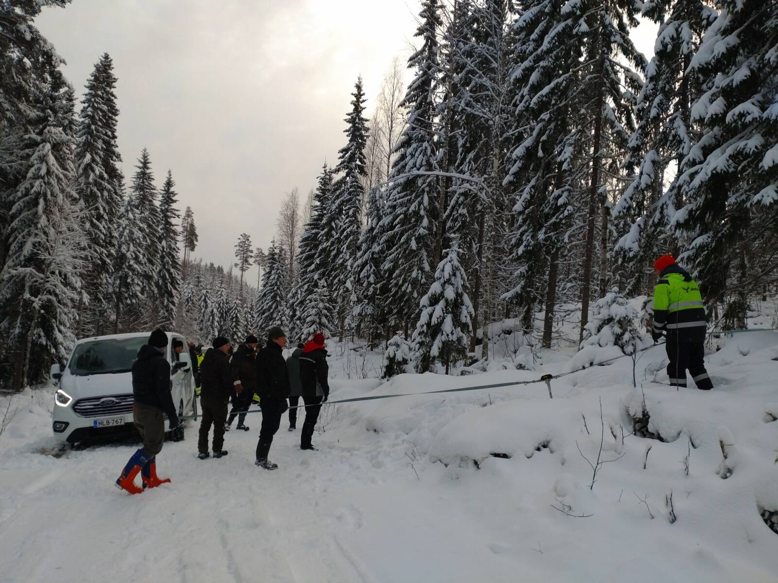 Ihmisiä seisomassa ulkona talvella tien reunassa olevan valkoisen auton vieressä.