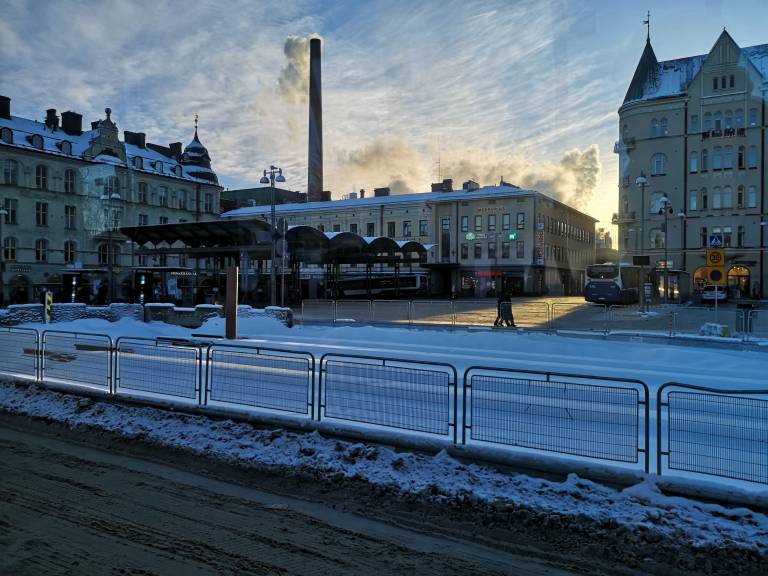 Tramline next to Keskustori square, snow in the ground, silhouettes of buildings against the setting sun