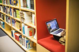 Kirjastossa hyllyissä kirjoja ja kannettava tietokone.