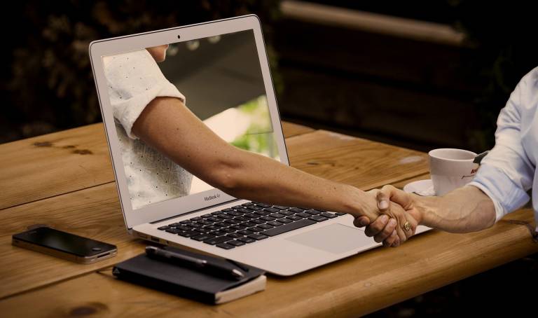 Hands shaking through a laptop screen.