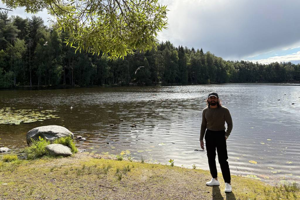 International student standing by lakeside in Hervanta, Tampere, surrounded by Finnish forest and nature.