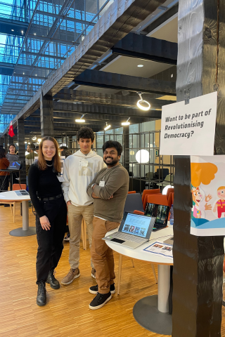 Three students at a networking event standing in front of a table.