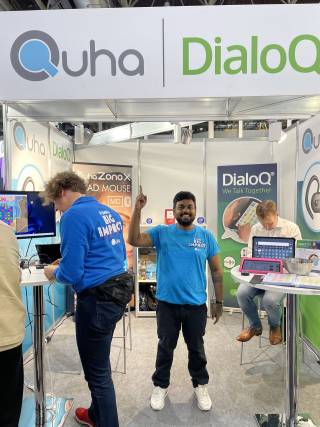 Two men in blue. A stall sign with the logo Quha. Decorations of various banners.