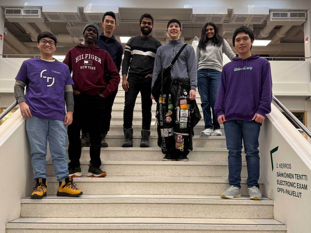 Seven international students posing on an indoor staircase at Tampere University.