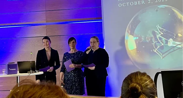 Kolme naista seisoo valkokankaan edessä pitämässä puheenvuoroa konferenssissa.