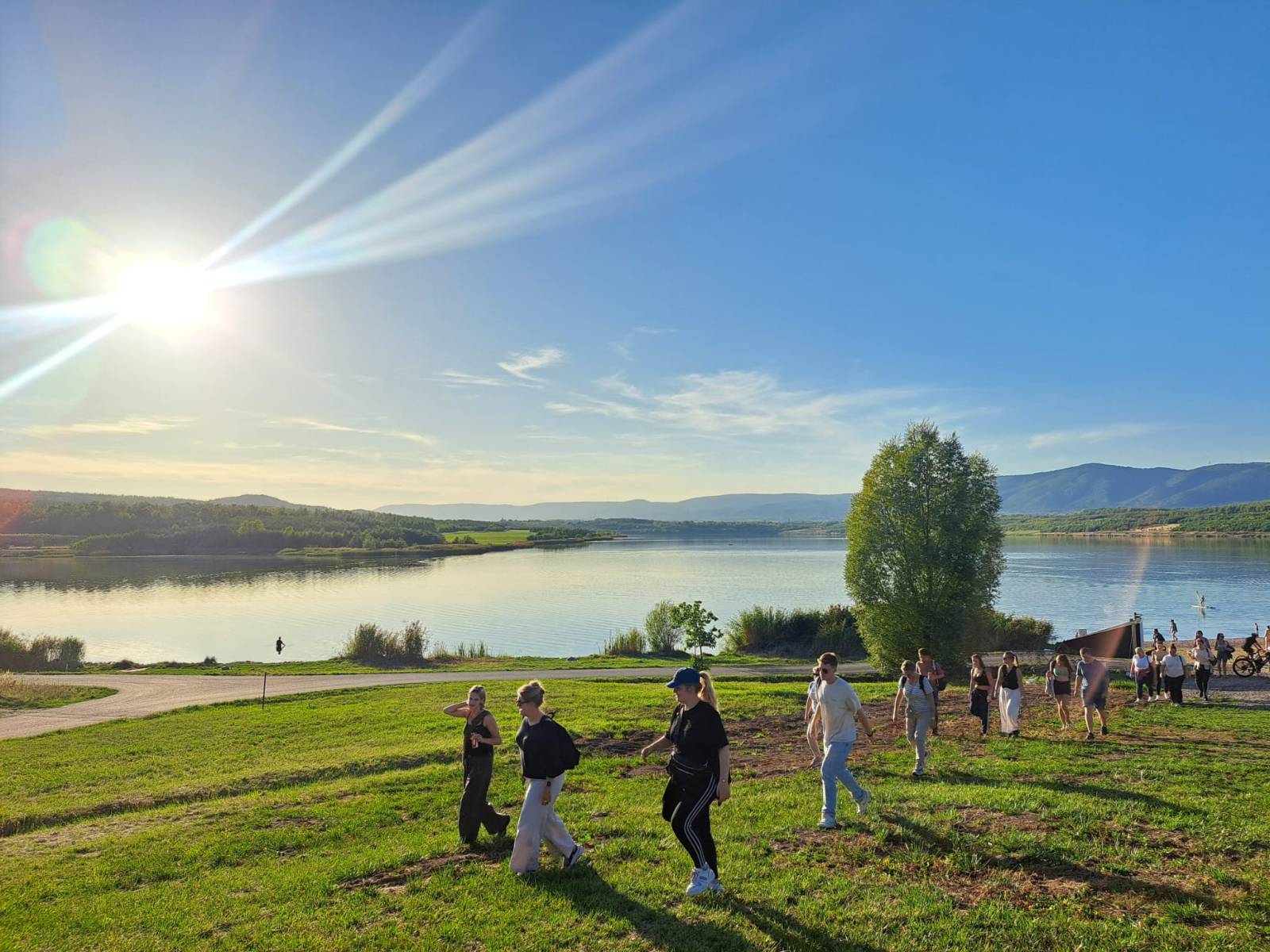 Taustalla järvi, edessä pellolla ryhmä käveleviä ihmisiä.