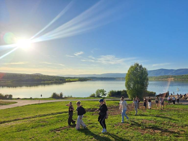 Taustalla järvi, edessä pellolla ryhmä käveleviä ihmisiä.