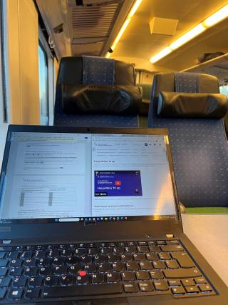 Etualalla tietokone ja taustalla junan penkit. 