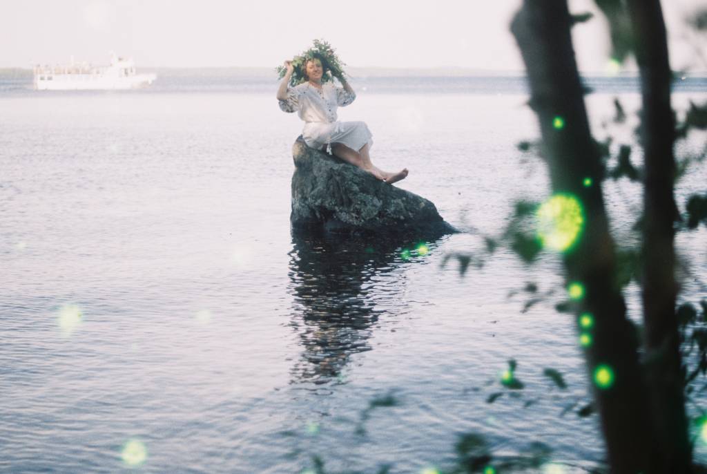 Valkoasuinen Mariia kiven päällä järvellä.