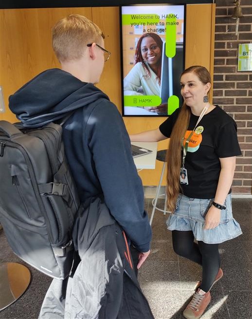 Iida ohjaamassa opiskelijaa aulassa.