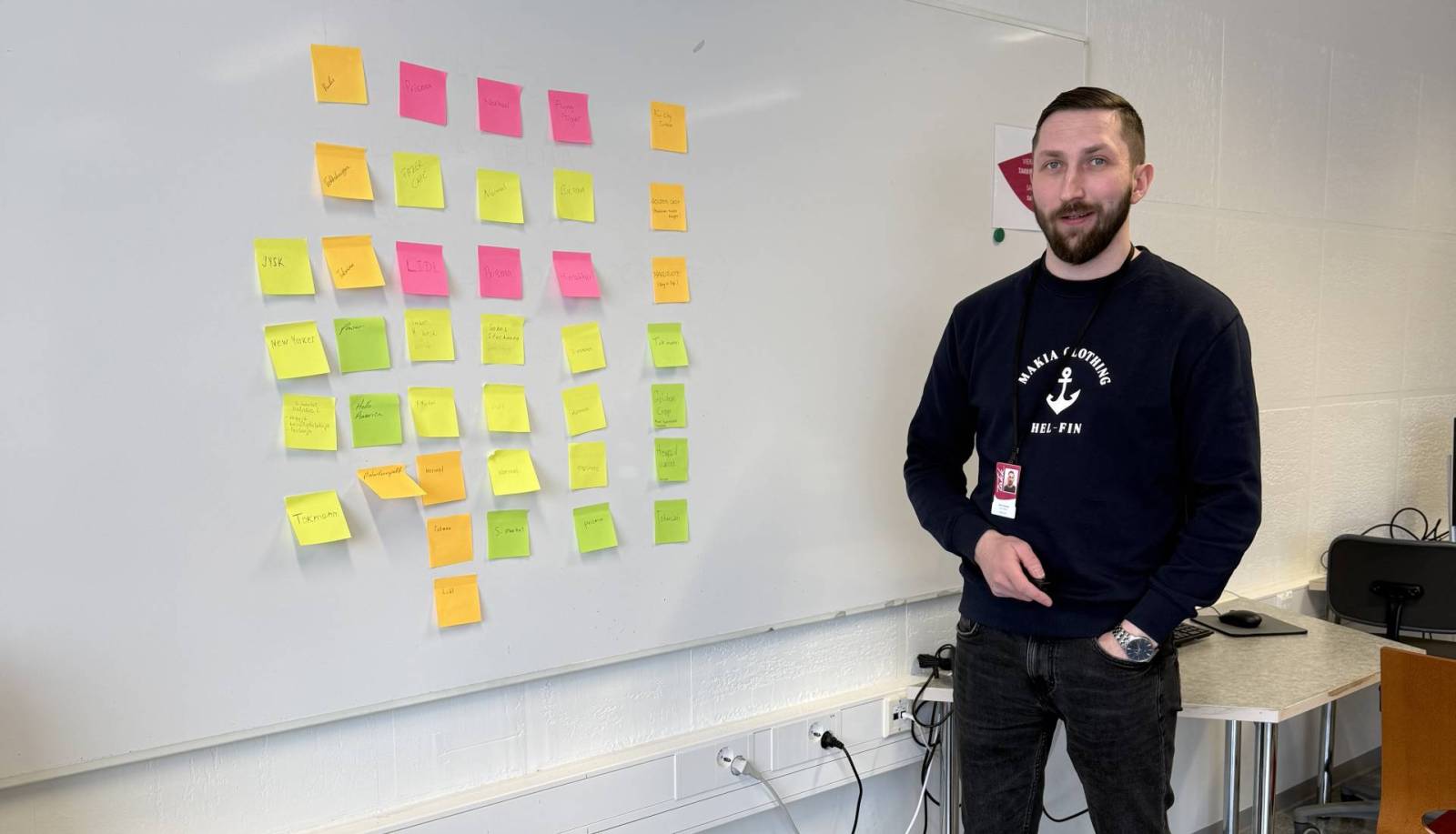 Jimi etualalla. Taustalla taulu, jossa värikkäitä tarralappuja.