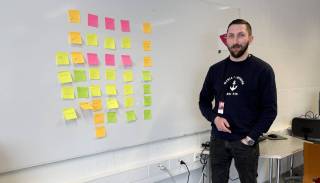 Jimi etualalla. Taustalla taulu, jossa värikkäitä tarralappuja.