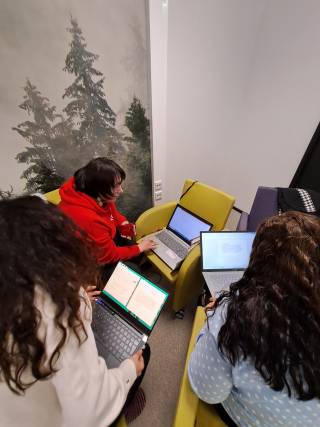 Kolme opiskelijaa tietokoneiden kanssa takaa kuvattuina.