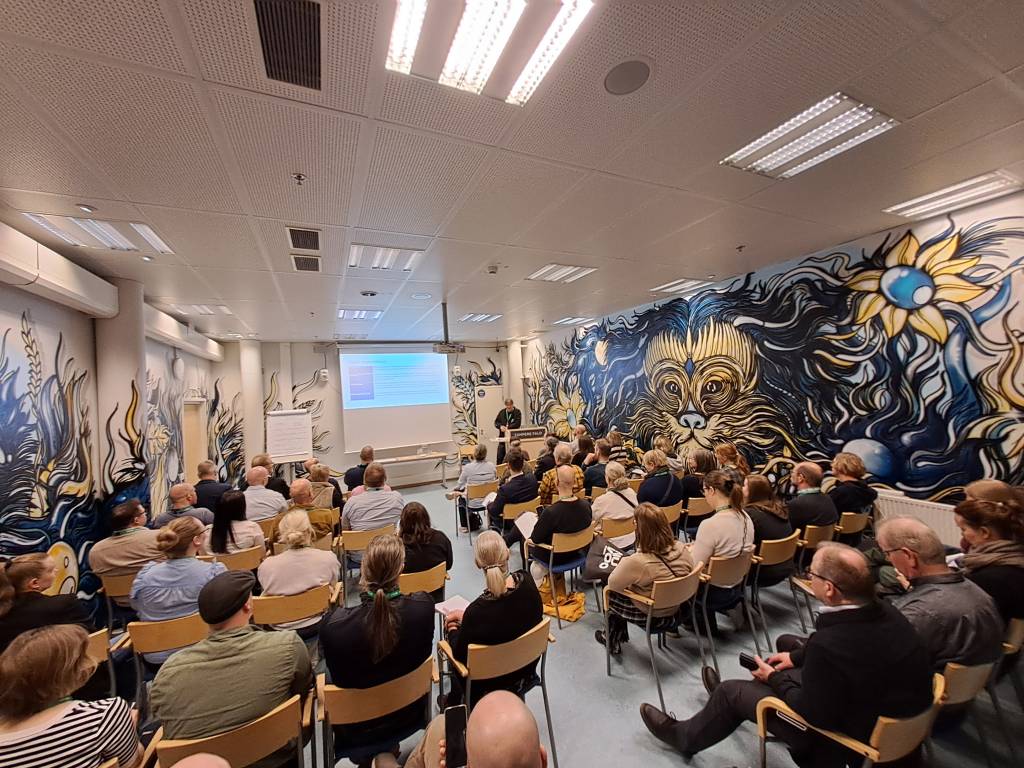 Salillinen ihmisiä kuuntelemassa esitystä.