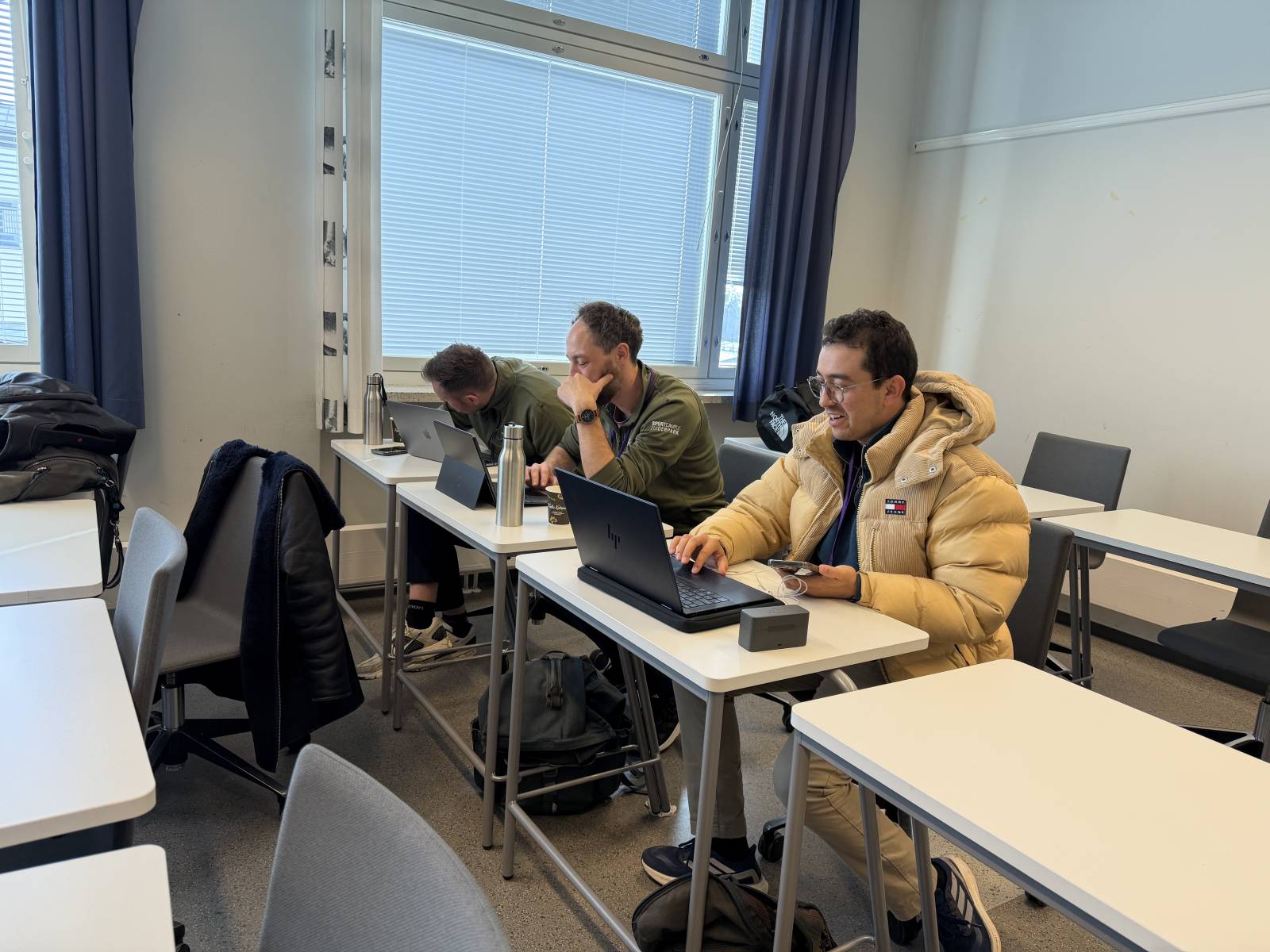 Kolme henkilöä istuu pulpeteissa.