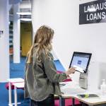 Naisoletettu opiskelija käyttää kirjaston lainauskonetta.