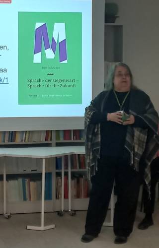 Image shows Dr. Nurmi standing next to the screen and holding a book