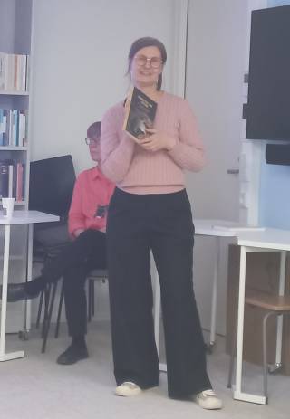 Image shows Dr. Ratilainen standing up and holding a book