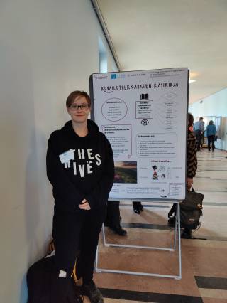 The image shows PhD researcher Mira Kainulainen standing next to the poster presenting her research