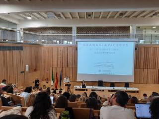 The image shows a large conference hall during the opening session, with the author Mikhail Shishkin standing on the left and the screen behind him showing a welcome message