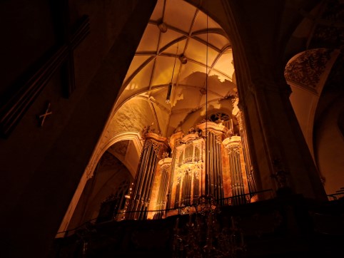 The high ceiling and the organ loft of the Graz Cathedral are lit with soft orange lightning in the otherwise dark church.