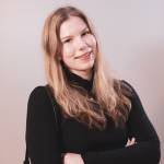 Hymyilevä nuori nainen mustassa paidassa, kädet rinnan päällä, katsoo kameraan.