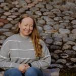 Hymyilevä nuori nainen istuu kivetyksen reunalla.