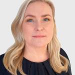 Hymyilevä vaaleahiuksinen nainen katsoaa kameraan.