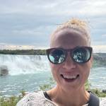 Hymyilevä nainen seisoo Niagaran putousten edessä.