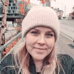 Hymyilevä nainen katsoo kameraan, taustalla on ruskan väreissä hehkuva lehtipuu.