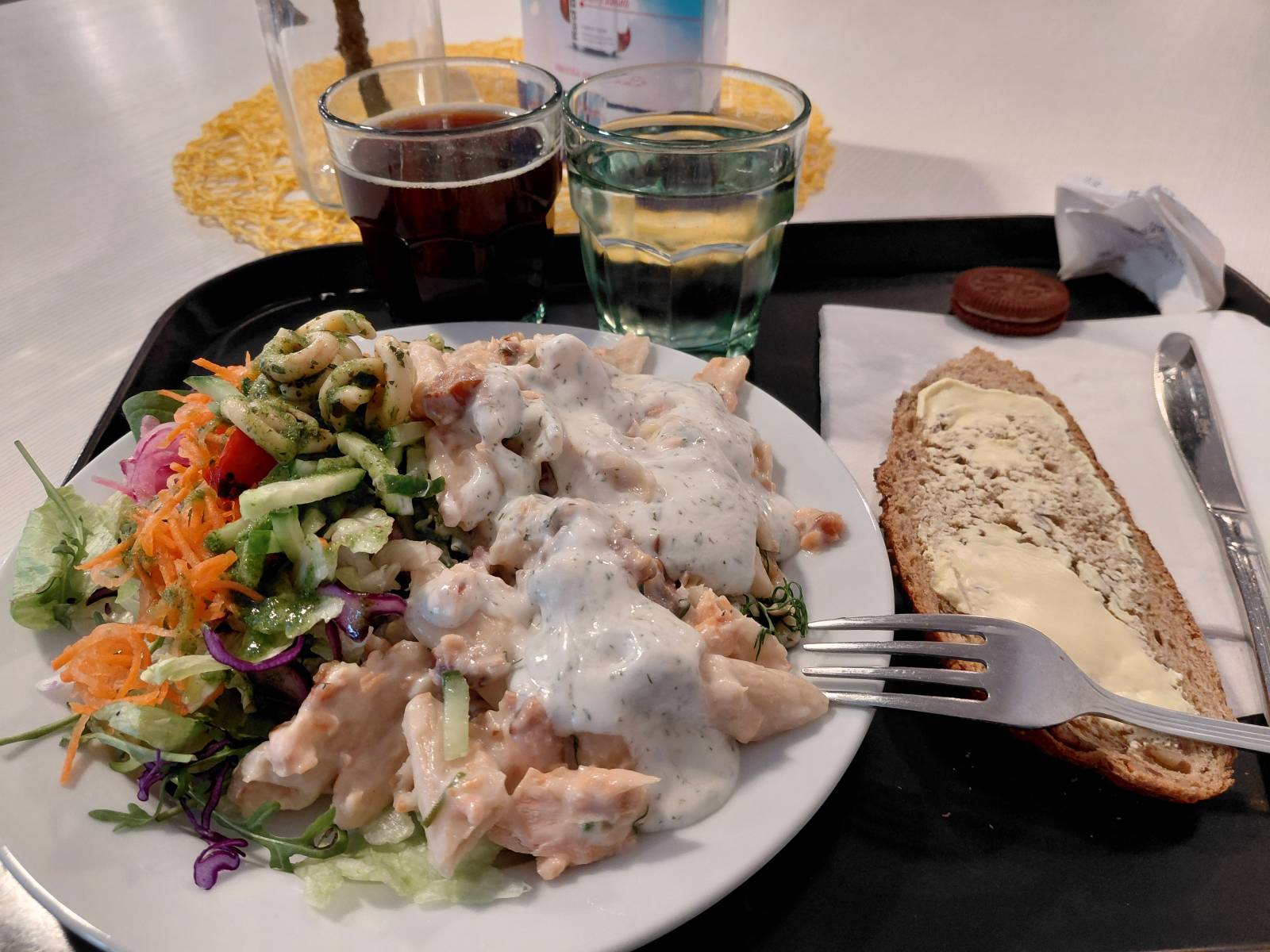 Tarjottimella värikäs ruoka-annos. Lasi kotikaljaa ja leipäsiivu.