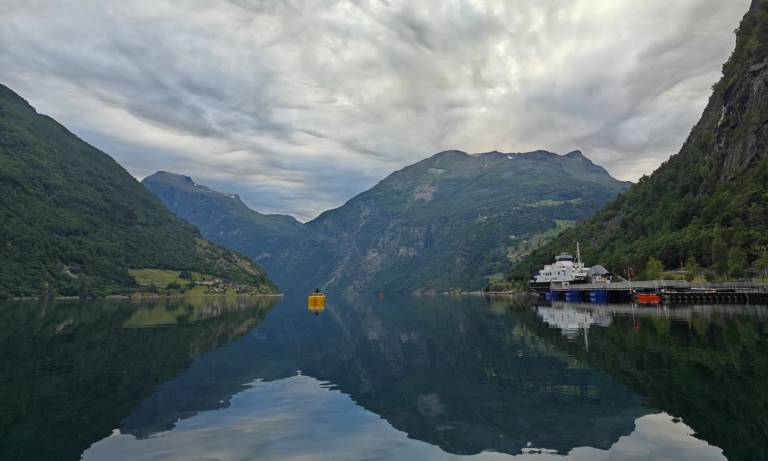 Image of a Geirangerfjord on a cloudy day. Sky is reflecting from the water.