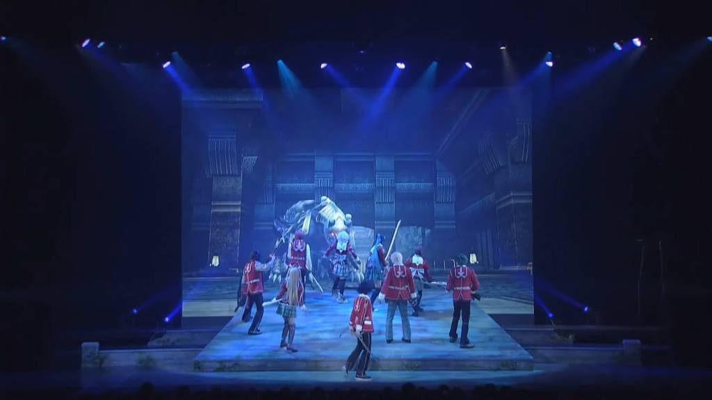 Group of students (actors) in the middle of a stage with a computer generated animation of a monster in the background center 