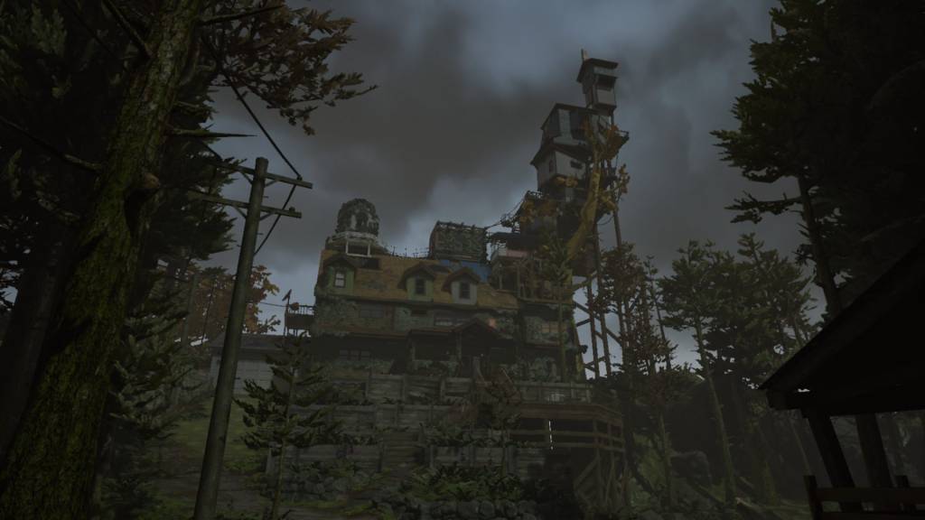 Eccentric looking, many storied house with a tall, towerlike structure on one side stands in the middle of a foresty area.