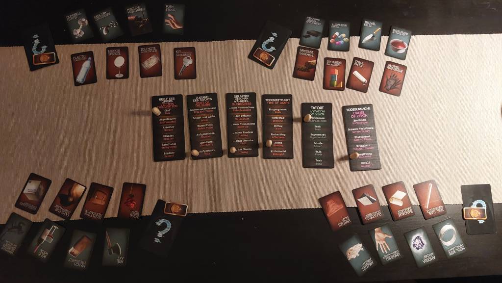 A dimly-lit table filled with various cards, cardboard tiles and tokens. Each player has 8 face-up cards, which are turned around for opposing players to see.