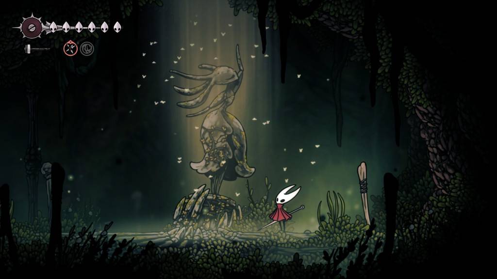 Hornet, in a luscious green area, looks up at a large, graceful statue of another bug.