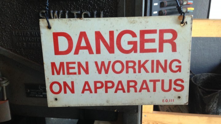 Sign saying danger, men working on apparatus.