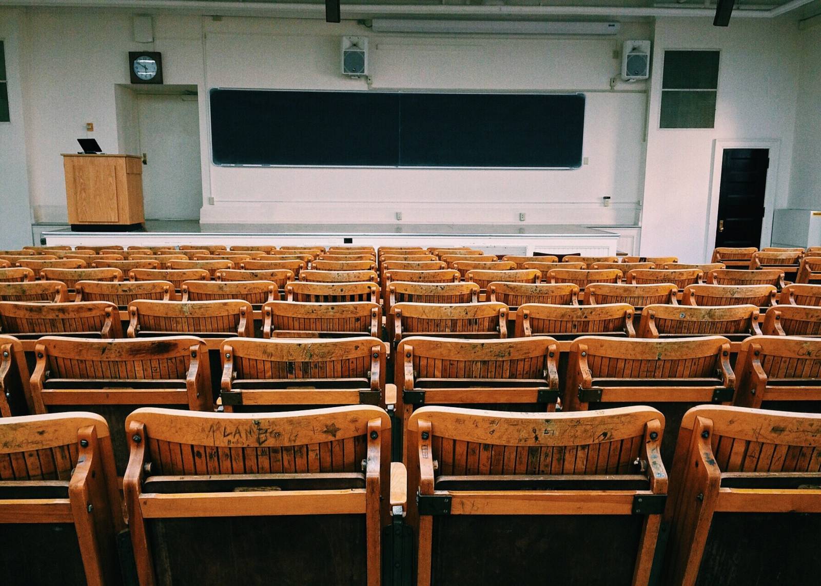 An auditorium full of empty wooden chairs and a blackboard in the front