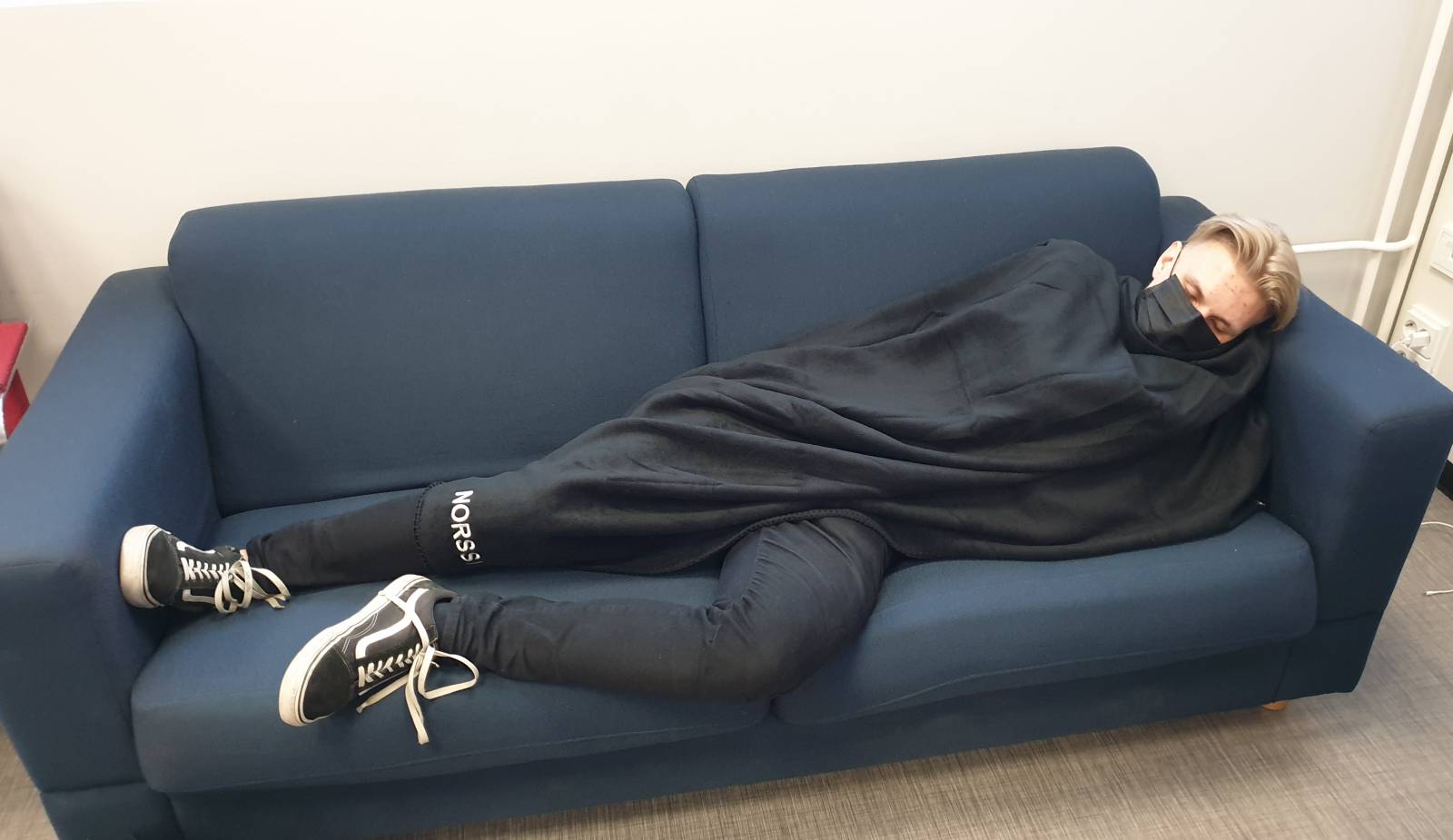 Opiskelija nukkuu sohvalla viltin alla Tampereen norssin lukiossa.
