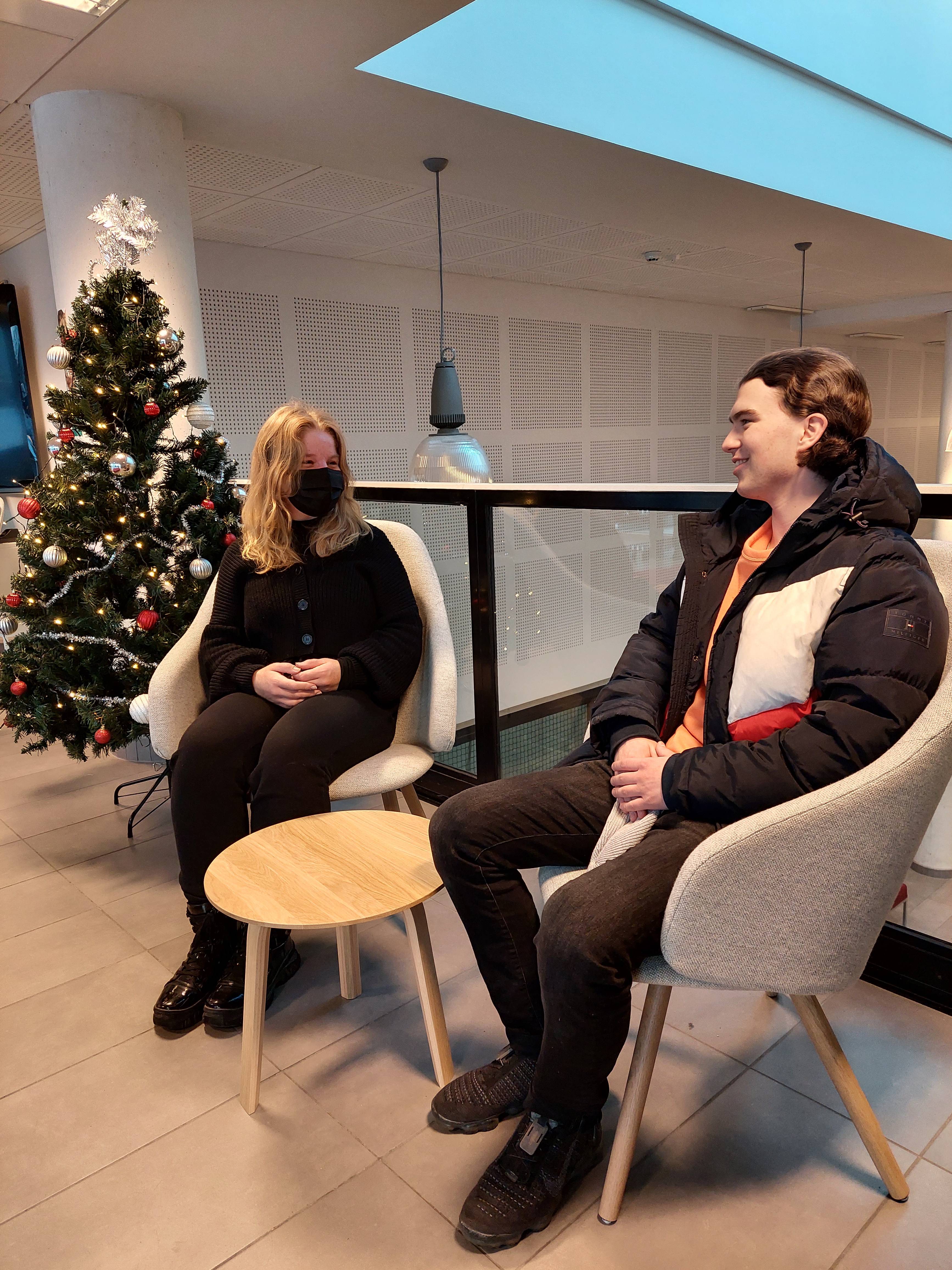 Kuva, jossa kaksi opiskelijaa istuu aulassa uusilla tuoleilla joulukuusi vieressään.