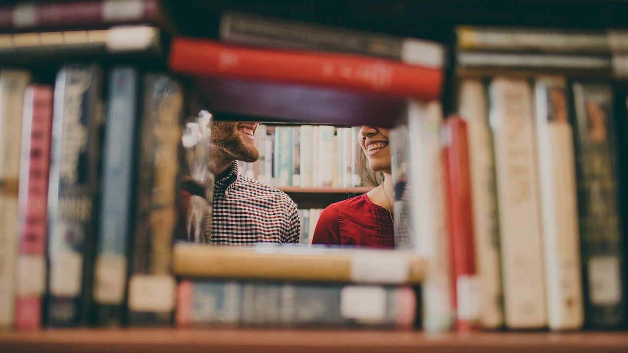 Kaksi ihmistä hymyilee toisilleen kirjahyllyjen välissä.